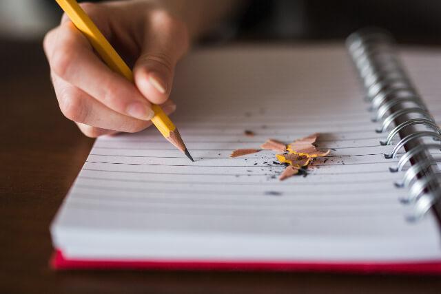 Hand writing in notebook with pencil, pencil shavings are scattered on paper